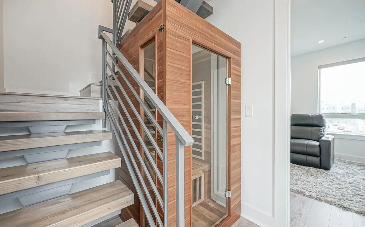A modern staircase with wooden steps and metal railings, leading to a room with a glass door and a view of the city.