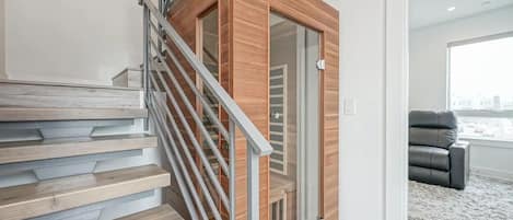 A modern staircase with wooden steps and metal railings, leading to a room with a glass door and a view of the city.