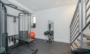 Uma academia em casa com barra de exercícios, supino, halteres e espelho.