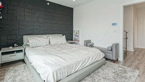 Una camera da letto moderna con un letto grande, un divano grigio, un tavolino e un'opera d'arte appesa al muro.