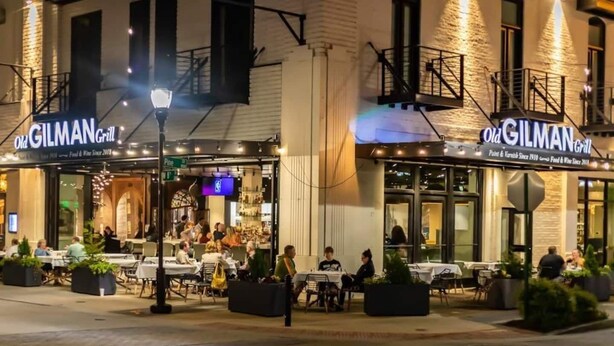 Restaurante com mesas ao ar livre, fachada de tijolos e letreiros iluminados.