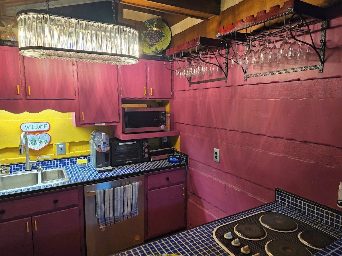 Una cocina con microondas, fregadero y estufa. Hay un cartel que dice 'Welcome' en la pared y una estantería para vinos sobre la encimera.