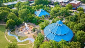 Vista aérea de um parque com uma fonte, um coreto e um edifício grande com telhado azul.