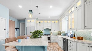 A modern kitchen with white cabinets, a blue island, and pendant lighting. - Harbor View Retreat with Heated Pool, Wraparound Decks & Sunset Vibes - Sunset Harbor - Roelens (Punta Gorda)