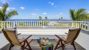 A wooden deck with two wicker chairs and a small table with two wine glasses, overlooking a beach with palm trees and sailboats. - Harbor View Retreat with Heated Pool, Wraparound Decks & Sunset Vibes - Sunset Harbor - Roelens (Punta Gorda)