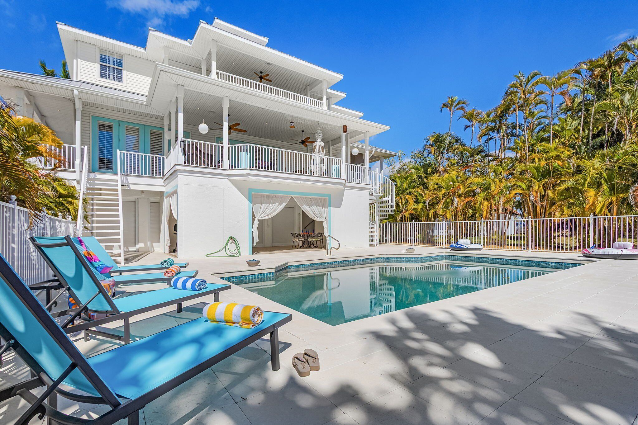Una casa grande y blanca con piscina, varios balcones y un jardín tropical.