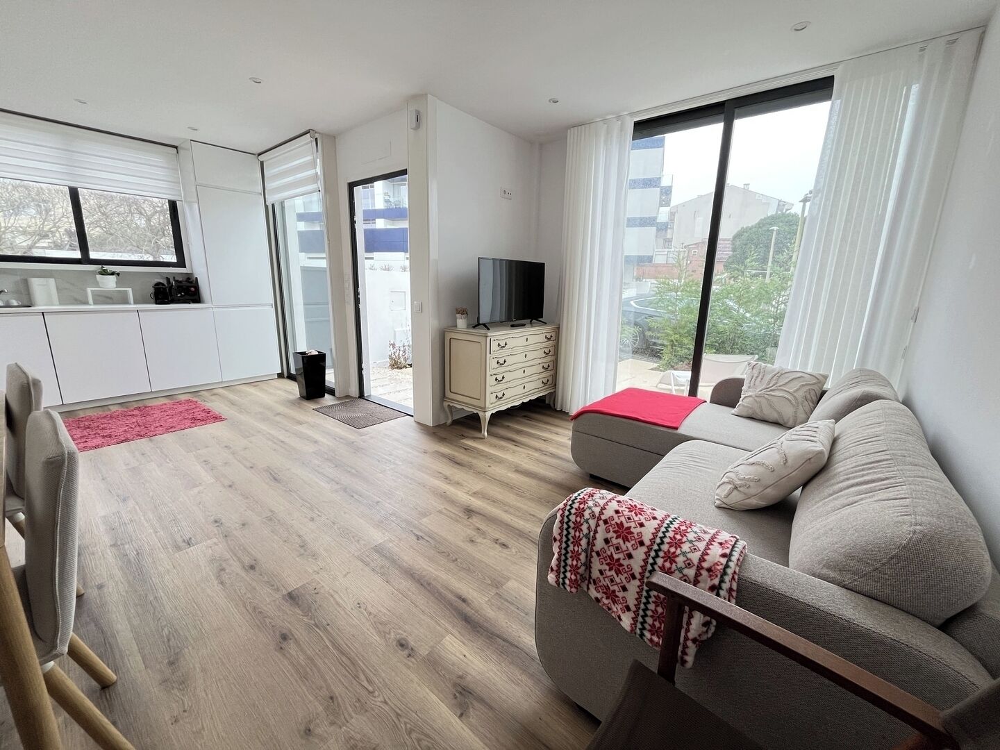 A modern living room with a sofa, a television, and a view of the outside.