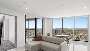 A modern living room with a sectional sofa, a dining table, and large windows offering a city view. - Level 42 Beachside 1BR Apartment with Ocean Views (Surfers Paradise)