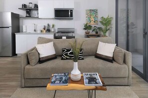 Ein modernes Wohnzimmer mit einer Couch, einem Couchtisch, Zeitschriften und einer Küche im Hintergrund.