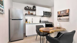 A compact kitchen with a stainless steel refrigerator, a microwave, and a stove. There is a dining area with a wooden table and two black chairs. - Apartment with Large Outdoor Balcony (Panamá)