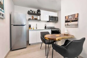 A compact kitchen with a stainless steel refrigerator, a microwave, and a stove. There is a dining area with a wooden table and two black chairs. - Apartment with Large Outdoor Balcony (Panamá)