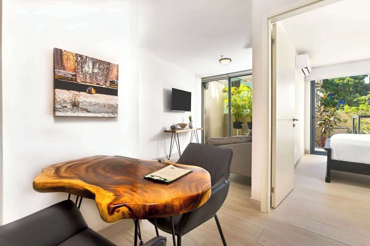 Habitación de hotel moderna con una mesita de centro de madera, televisor de pantalla plana, cama y balcón con vistas a zonas verdes.
