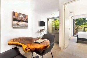 Ein modernes Hotelzimmer mit einem Holztisch, einem Flachbildfernseher, einem Bett und einem Balkon mit Blick auf Grünflächen.