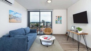 Una sala de estar moderna con un sofá azul, una mesa de centro redonda y un televisor sobre un mueble de madera.