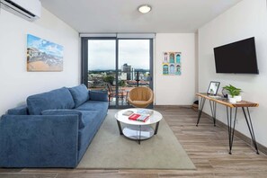 Una sala de estar moderna con un sofá azul, una mesa de centro redonda y un televisor sobre un mueble de madera.