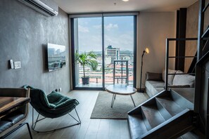 A modern living room with a sofa, a chair, a small table, a potted plant, and a view of the city through large windows. - Penthouse con piscina y vistas en Centro Histórico (Panamá)