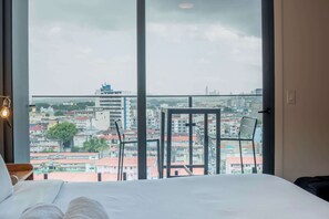 A hotel room with a large window offering a city view, a bed, and a chair. - Penthouse con piscina y vistas en Centro Histórico (Panamá)
