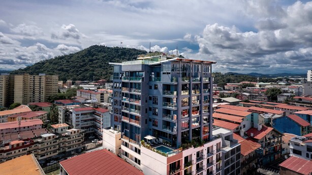 A multi-story building with balconies, surrounded by other buildings, under a partly cloudy sky. - Apartment Upper Level in Casco View (Panamá)