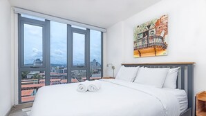 A hotel room with a large bed, a city view, and a painting on the wall. - Apartment Upper Level in Casco View (Panamá)