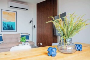 Een woonkamer met een bank, een bijzettafeltje met een vaas groene planten, en een televisie op een meubel.