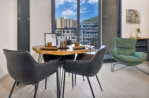 Una habitación moderna con una mesa redonda, sillas negras, un sillón verde y un ventanal con vistas a la ciudad.