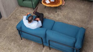 Un'area salotto esterna moderna con divani verdi e un tavolo rotondo, circondata da piante in vaso.