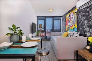 A modern living room with a sofa, dining table, and a large window. - Upper-Level Apartment with City Views (Panama City)