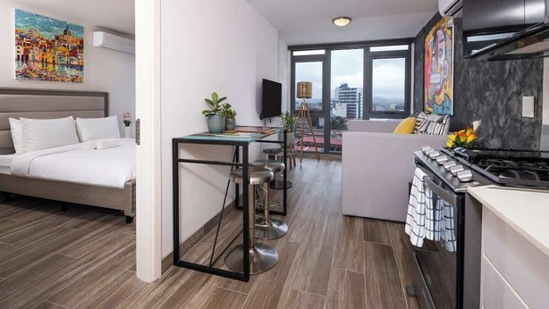 Una camera d'albergo moderna con un letto, angolo cottura e zona pranzo con tavolo e sedie.