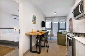 A compact hotel room with a bed, a small dining area, a kitchenette, and a large window providing natural light. - Casco View Life. 1 Bedroom (Panamá)
