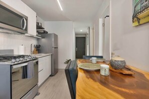A modern kitchen with stainless steel appliances, a wooden dining table with chairs, and a view into the adjacent dining area. - Casco View Life. 1 Bedroom (Panamá)