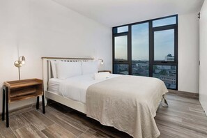 Ein modernes Schlafzimmer mit großem Fenster, einem Bett, einem Nachttisch und einem Beistelltisch.
