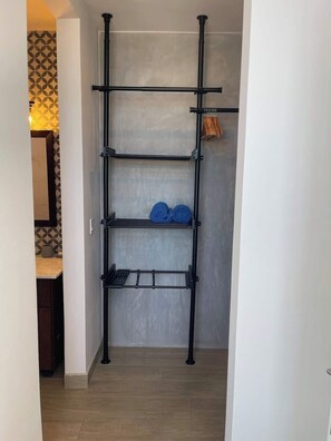 A metal shelving unit with three shelves, a wooden floor, and a patterned wall in the background. - Two-Level Penthouse | Bay & Cerro Ancón Views (Panama City)