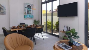 A modern dining area with a table set for four, surrounded by chairs, a television mounted on the wall, and a large window offering a view of buildings. - Ground Floor Terrace Apartment (Panama City)
