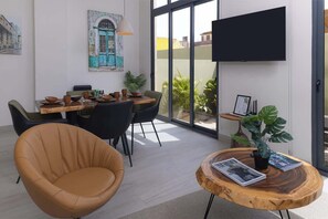 A modern dining area with a table set for four, surrounded by chairs, a television mounted on the wall, and a large window offering a view of buildings. - Ground Floor Terrace Apartment (Panama City)