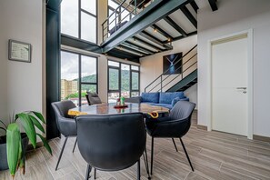 Ein modernes Wohnzimmer mit einem Holzessttisch, schwarzen Stühlen, einem blauen Sofa und einer Treppe, die in eine obere Ebene führt.