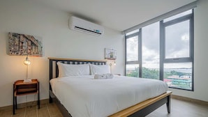 A modern hotel room with a large bed, a nightstand, an air conditioning unit, and a large window offering a view of the city. - Two-Level Loft with Large Terrace & Bay Views (Panama City)