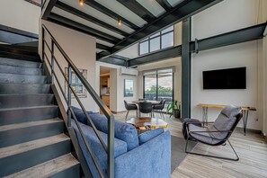 Ein modernes Interieur mit einer Treppe, einem blauen Sofa, einem Essbereich und einem an der Wand befestigten Fernseher.