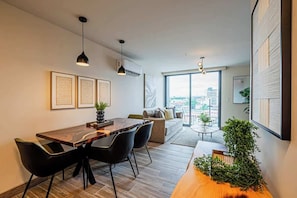A modern living room with a dining area, large windows, and a view of the city. - Jr. Apartment Upper Level in Casco View (Panamá)