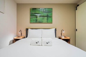 A hotel room with a bed, two bedside tables with lamps, a painting on the wall, and towels with a monogram. - Jr. Apartment Upper Level in Casco View (Panamá)