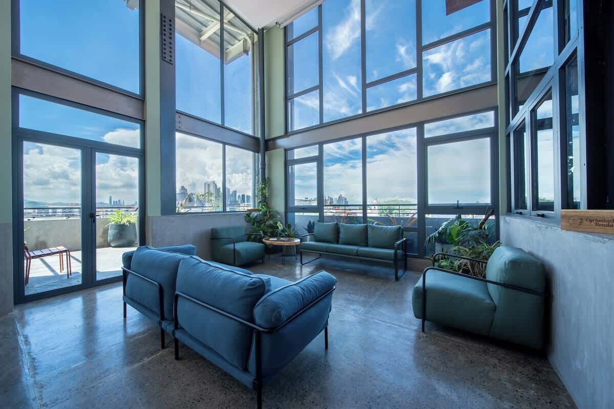 A spacious room with large windows, a blue sofa set, and a view of a city skyline.