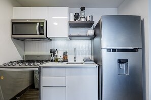 Eine kleine Küche mit Gasherd, Mikrowelle, Kühlschrank und Wasserspender.