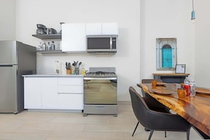 A modern kitchen with white cabinetry, a microwave, a stove, and a dining area with a wooden table and chairs. - Ground Floor Terrace Apartment (Panamá)