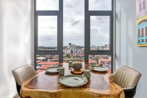 Ein Esstisch mit Tellern und einer Schüssel, mit Blick auf eine Stadtlandschaft durch große Fenster.