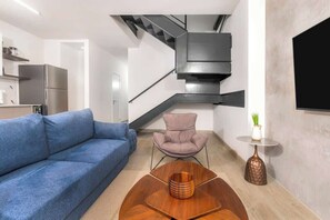 A modern living room with a blue sofa, a wooden coffee table, a pink chair, and a small table with a vase. - Penthouse with dual balconies and city views (Panama City)