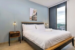 A bedroom with a bed, a bedside table, a wall-mounted light, and a window with a view. - Penthouse with dual balconies and city views (Panama City)