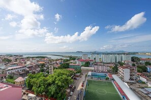 A coastal cityscape with a mix of residential and commercial buildings, a large green sports field, and a view of the sea. - Penthouse with Amador bay views and dual balconies (Panama City)
