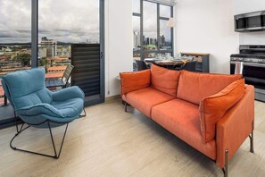 A modern living room with a sofa, a chair, and a dining area with a table and chairs. - City View Penthouse Suite (Panamá)