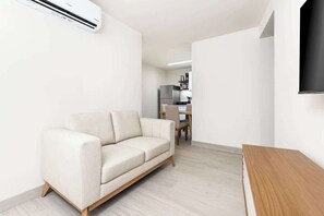 Ein modernes Wohnzimmer mit einer Couch, einem Holztisch und einer Küche im Hintergrund.