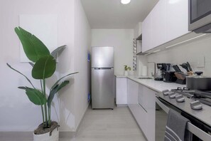 Eine moderne Küche mit weißen Schränken, einem Edelstahl-Kühlschrank, einem Gasherd und einem Topfpflanze.