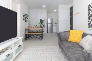 Ein Wohnzimmer mit grauem Sofa, Flachbildfernseher, Couchtisch und einem gemusterten Teppich.